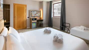 Ein Hotelzimmer mit zwei Betten, einem Schreibtisch, einer kleinen Kühlbox und einem Fenster mit Vorhängen.