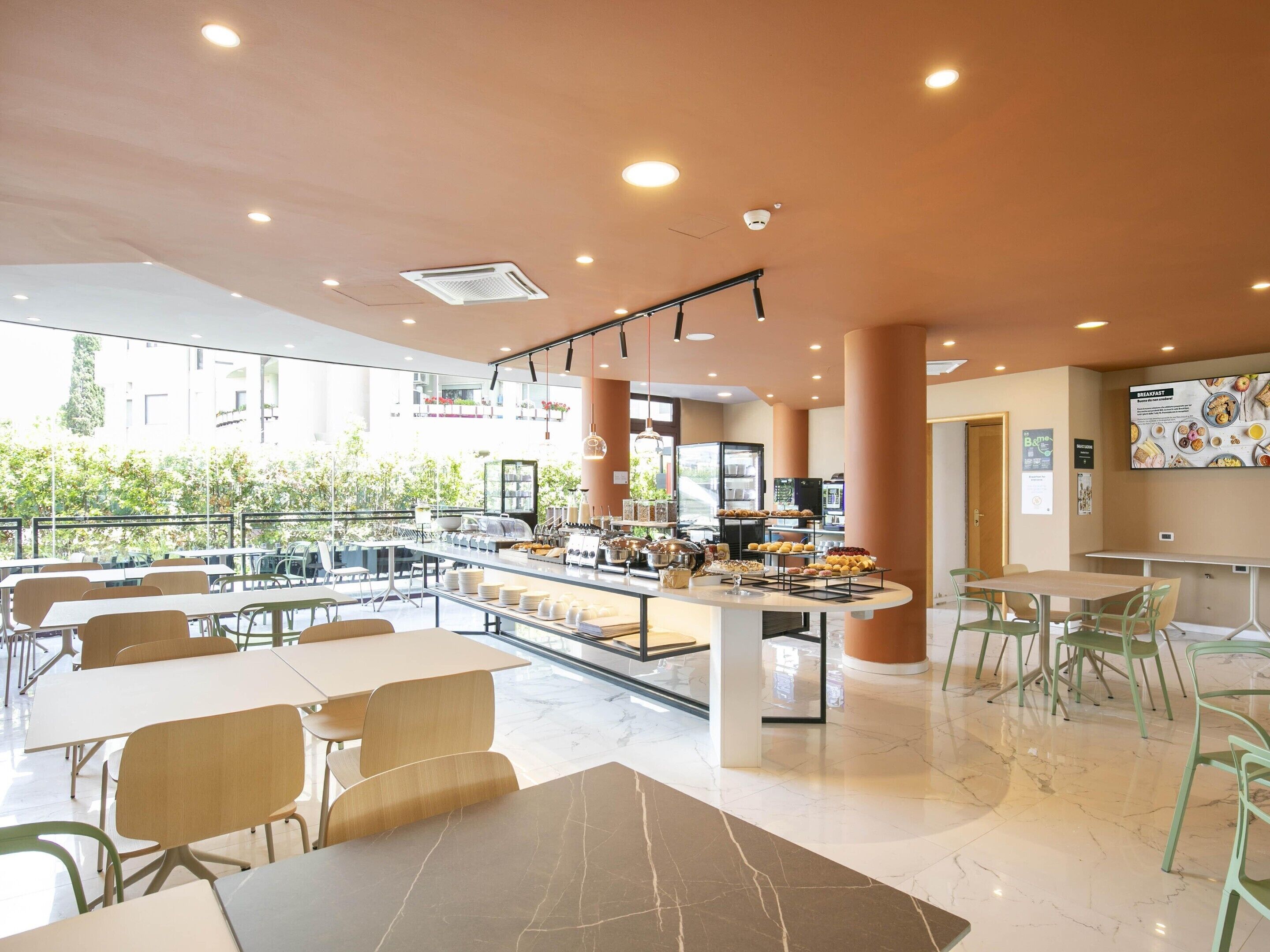 A modern cafe with a central counter, seating area, and a view of the outdoors.