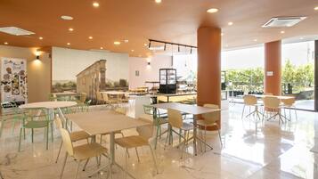 Un'ampia sala da pranzo con pavimento in marmo, diversi tavoli e sedie, e un grande murale sulla parete.