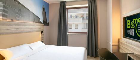 Une chambre d’hôtel avec un grand lit, un bureau avec une chaise, une télévision et une fresque représentant un bâtiment sur le mur.