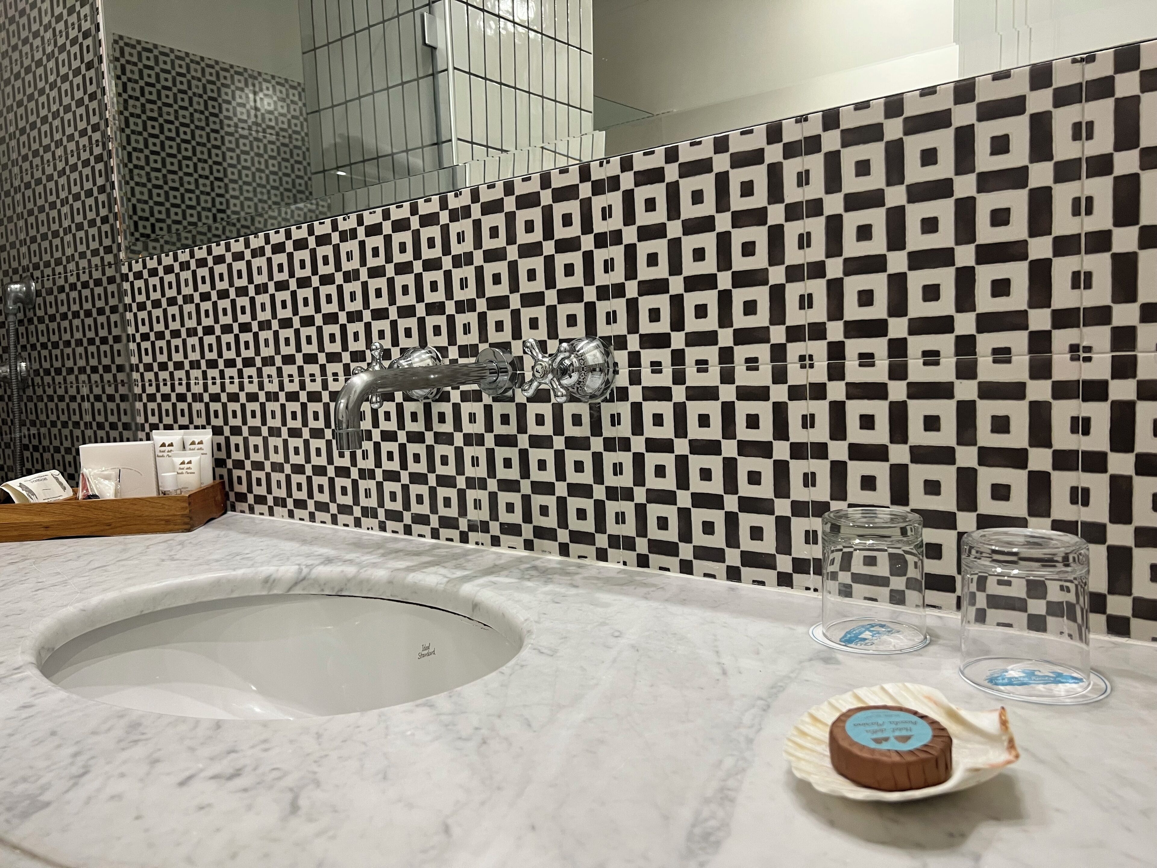 A bathroom with a checkered tile backsplash, a sink with a marble countertop, and toiletries on the counter.