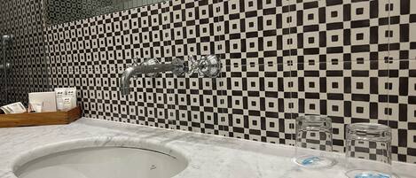 A bathroom with a checkered tile backsplash, a sink with a marble countertop, and toiletries on the counter.