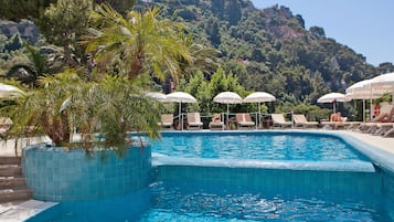 Relax by the serene pool surrounded by lush greenery and a picturesque mountain view.