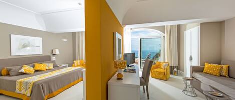 A modern hotel room with a bed, a desk, a chair, and a sofa. There is a large window with a view of the ocean.