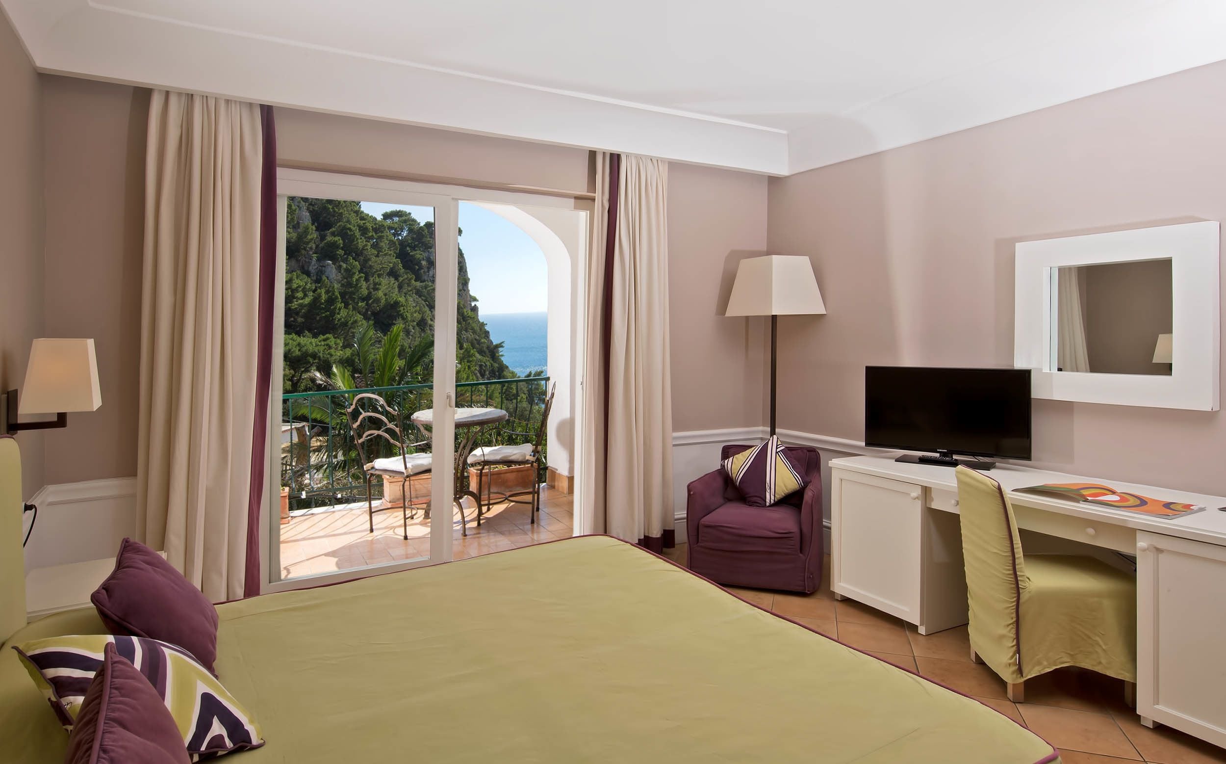 Habitación de hotel con cama, escritorio, televisión y balcón con vista al mar.