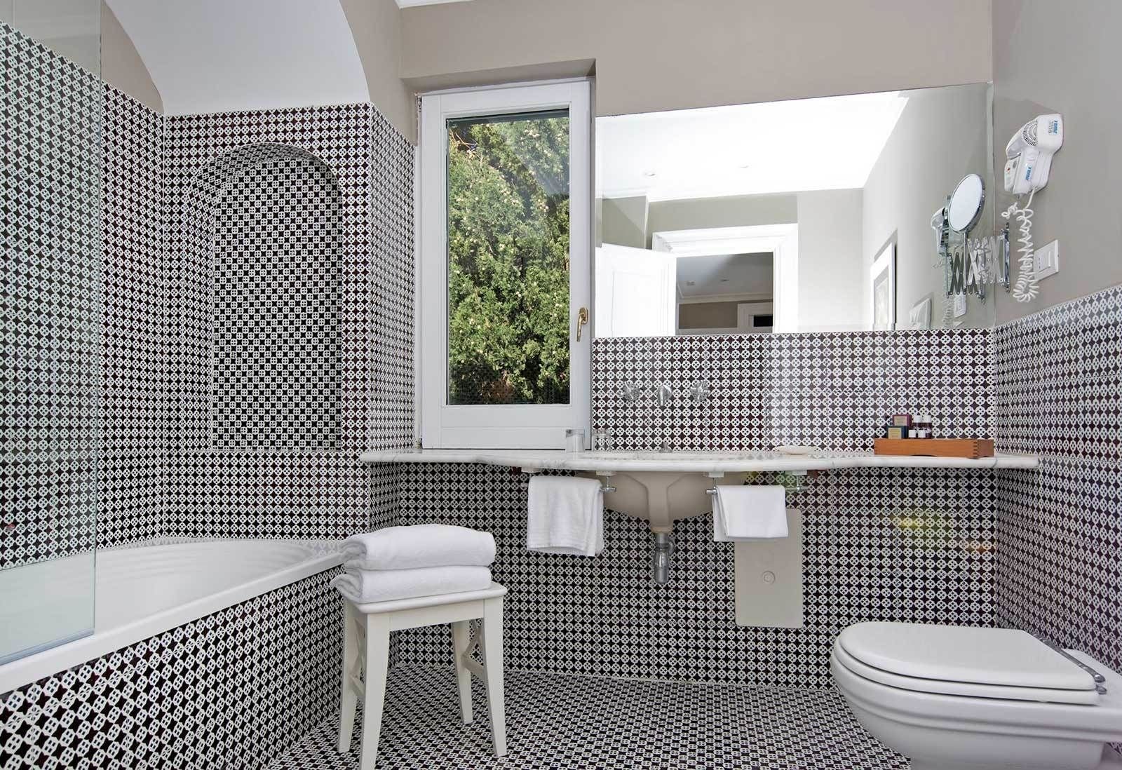 Un baño con azulejos blancos y negros estampados, un lavamanos blanco, un espejo y un inodoro.
