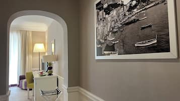 A hallway with a framed black and white photograph of a coastal town, a desk with a lamp, and a chair.