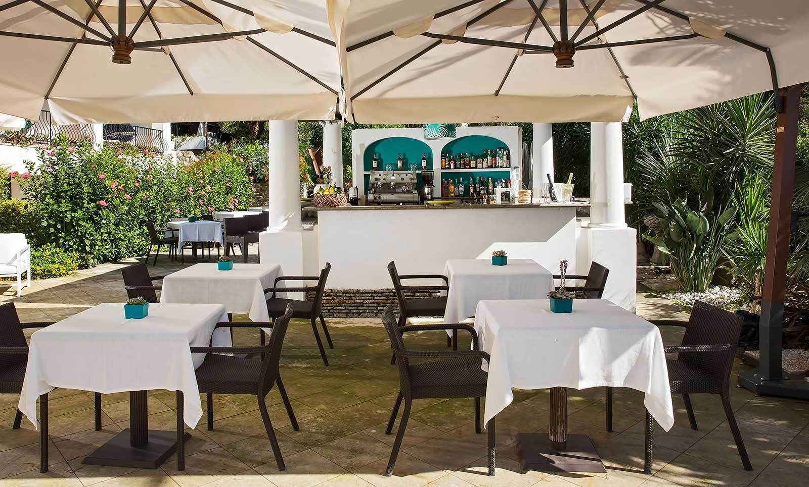Une terrasse extérieure avec des tables et des chaises, un coin bar et une végétation luxuriante en arrière-plan.
