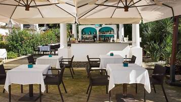 Une terrasse extérieure avec des tables et des chaises, un coin bar et une végétation luxuriante en arrière-plan.