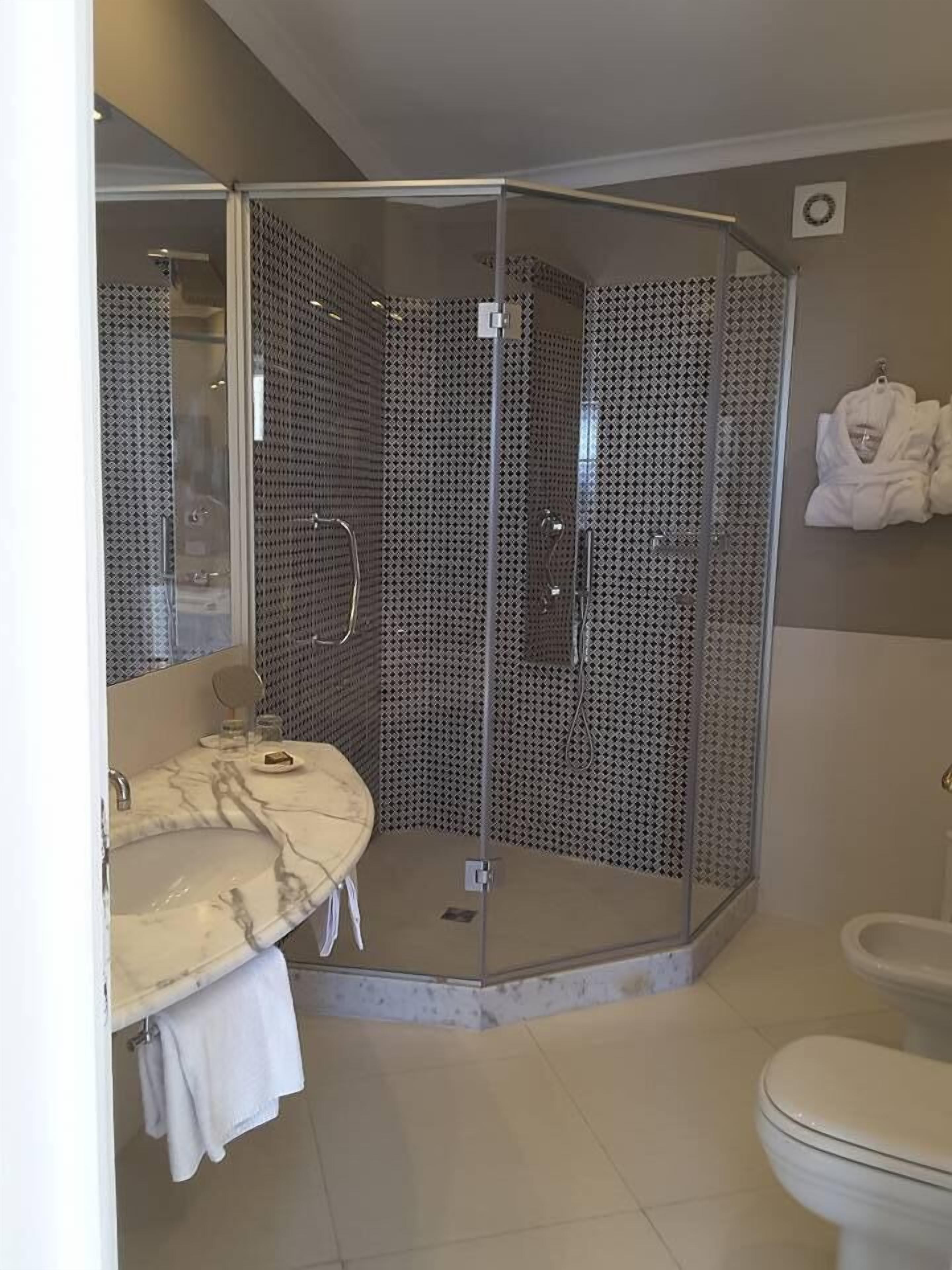 A modern bathroom with a glass-enclosed shower, a marble sink, and a toilet.