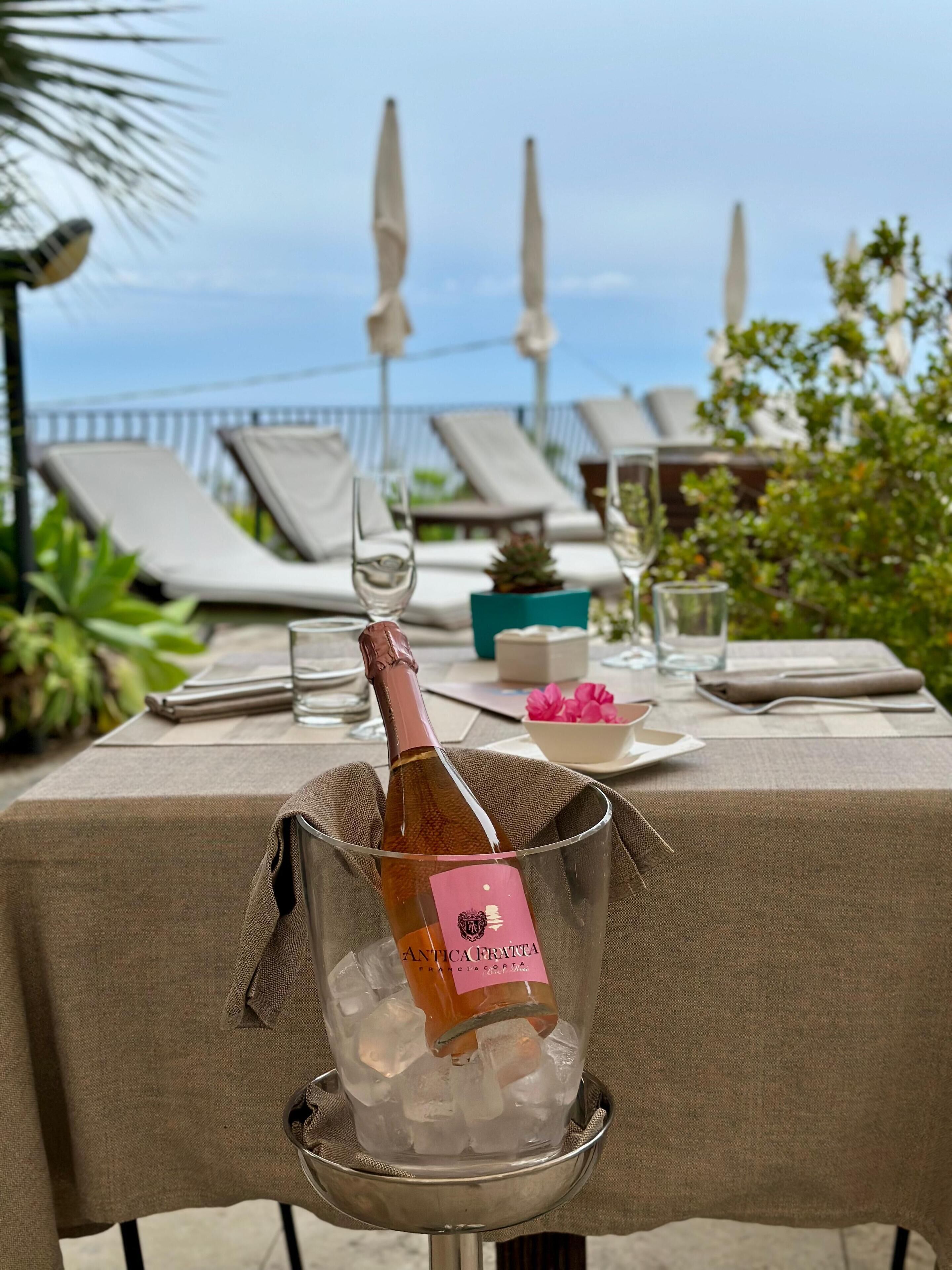 Ein gedeckter Tisch mit einem Essen, eine Flasche Antica Franca Wein in einem Kübel, umgeben von Tellern, Gläsern und einer Blumenblume.