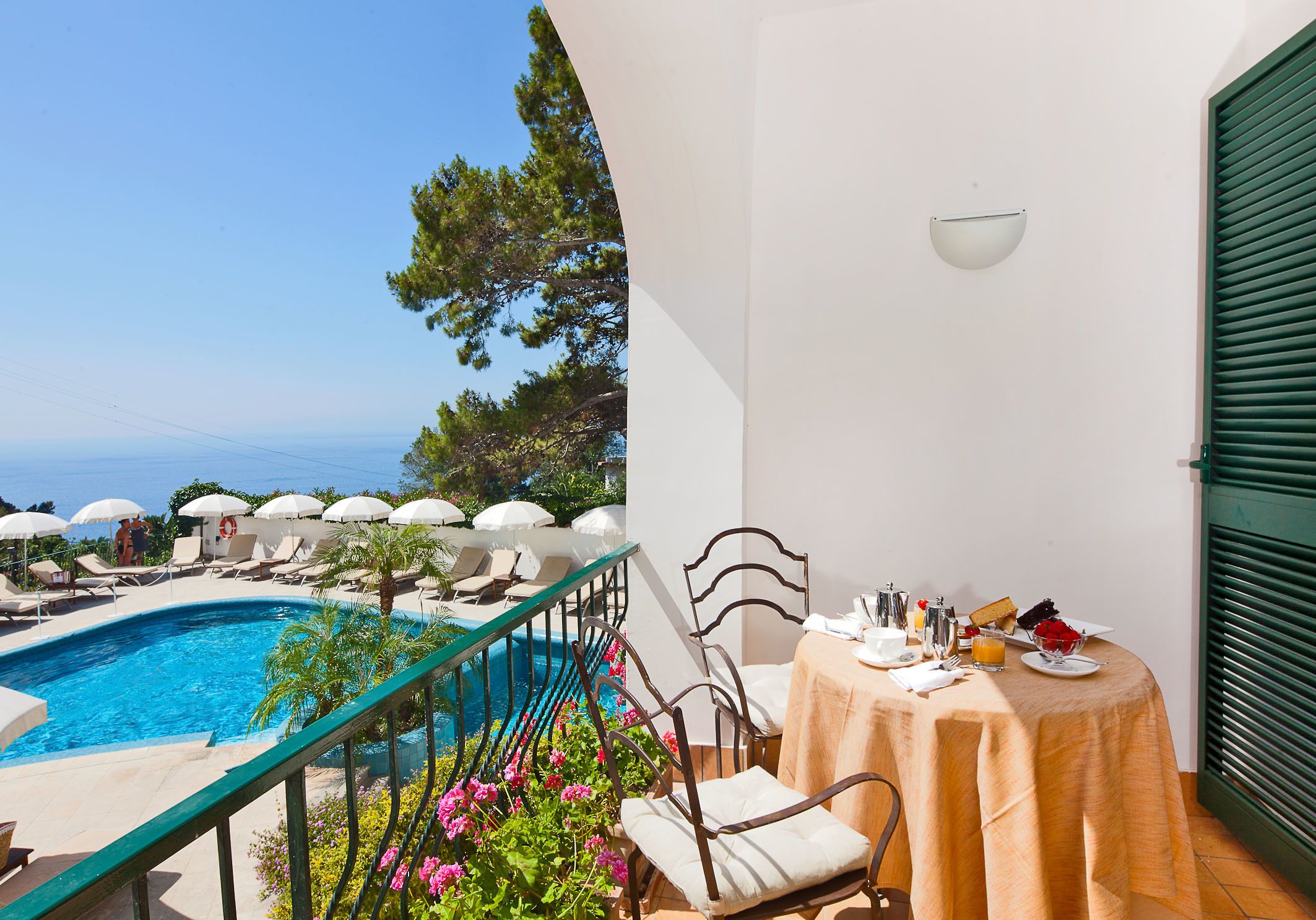 A balcony with a pool, chairs, and a table with breakfast items.