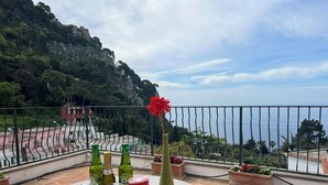 Una terraza con una mesa preparada para una comida, con vista a un paisaje montañoso y al mar.