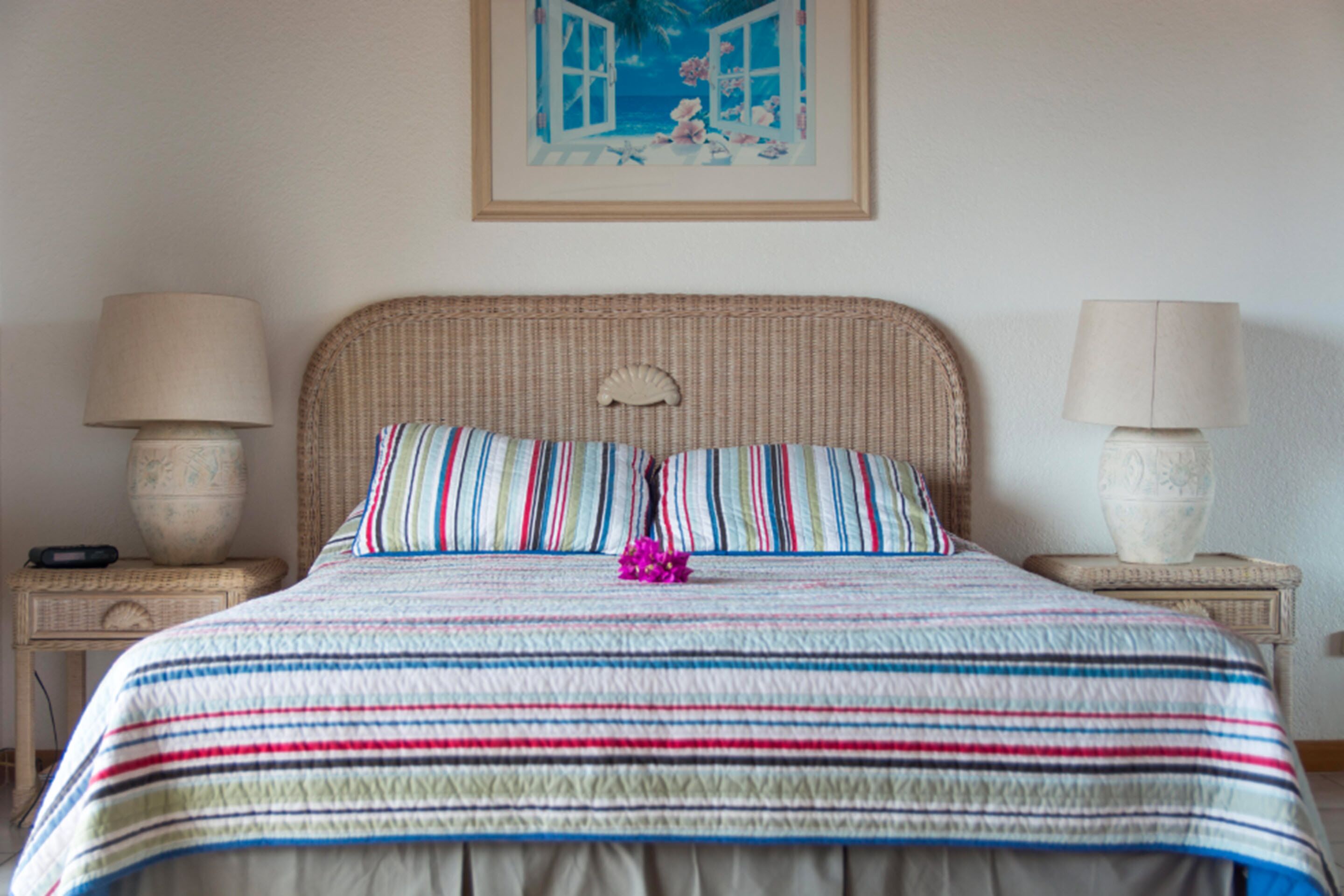 A bed with a striped bedspread, two pillows, and a decorative shell headboard. There are two bedside tables with lamps and a framed picture above the bed.