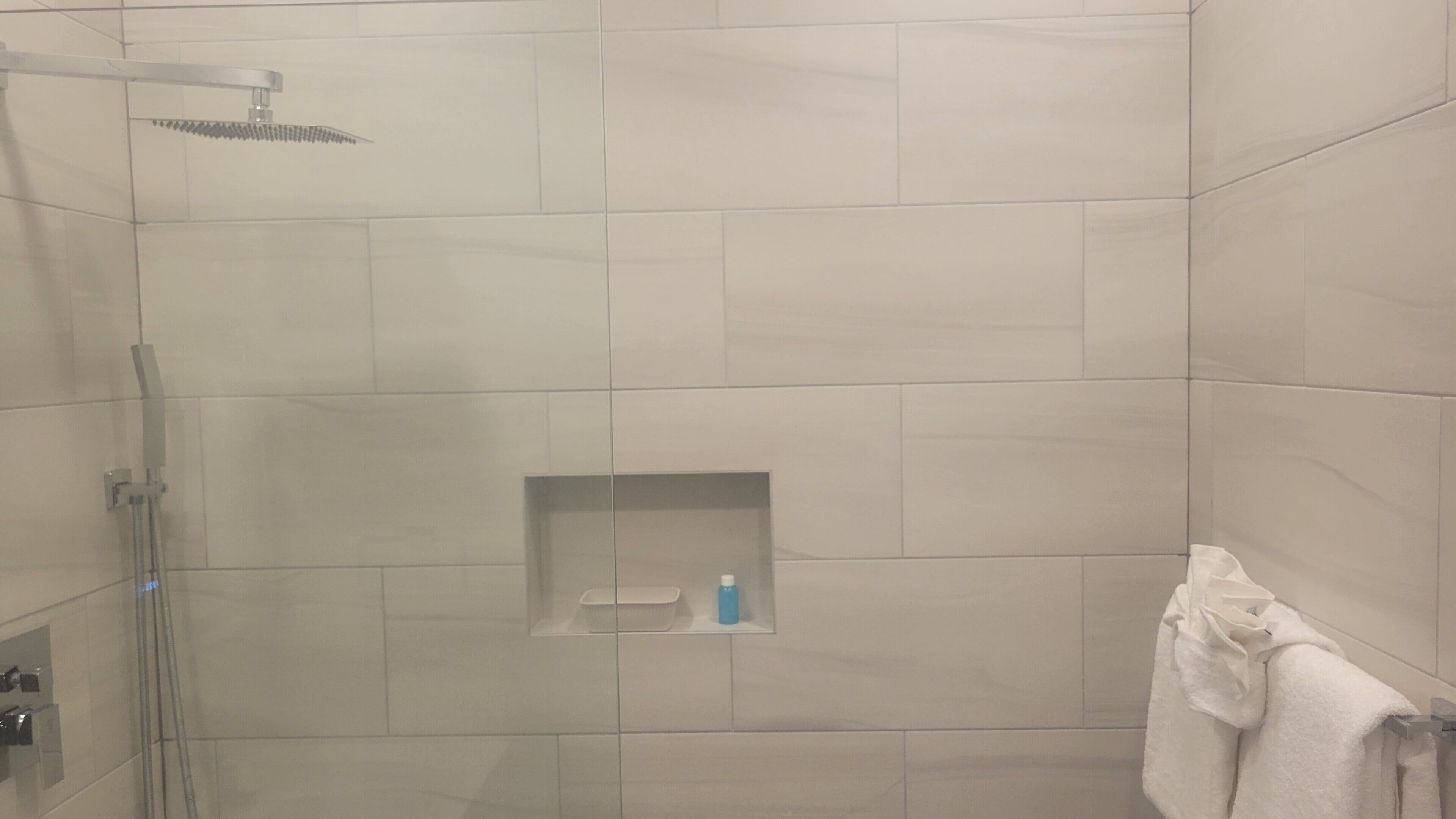 A shower area with a glass door, a towel rack, and a small shelf with toiletries.