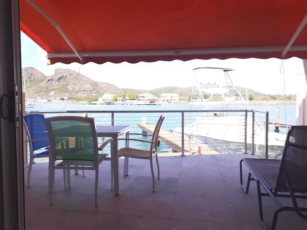 A balcony with a table and chairs, overlooking a marina with boats and a mountainous landscape.