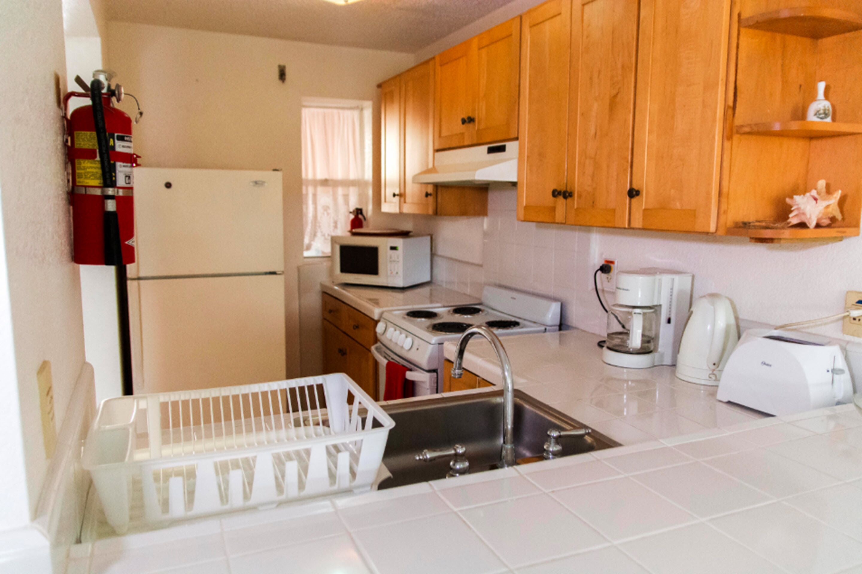 Una cocina con armarios de madera, un refrigerador blanco, un microondas, una estufa, un lavaplatos y una cafetera.