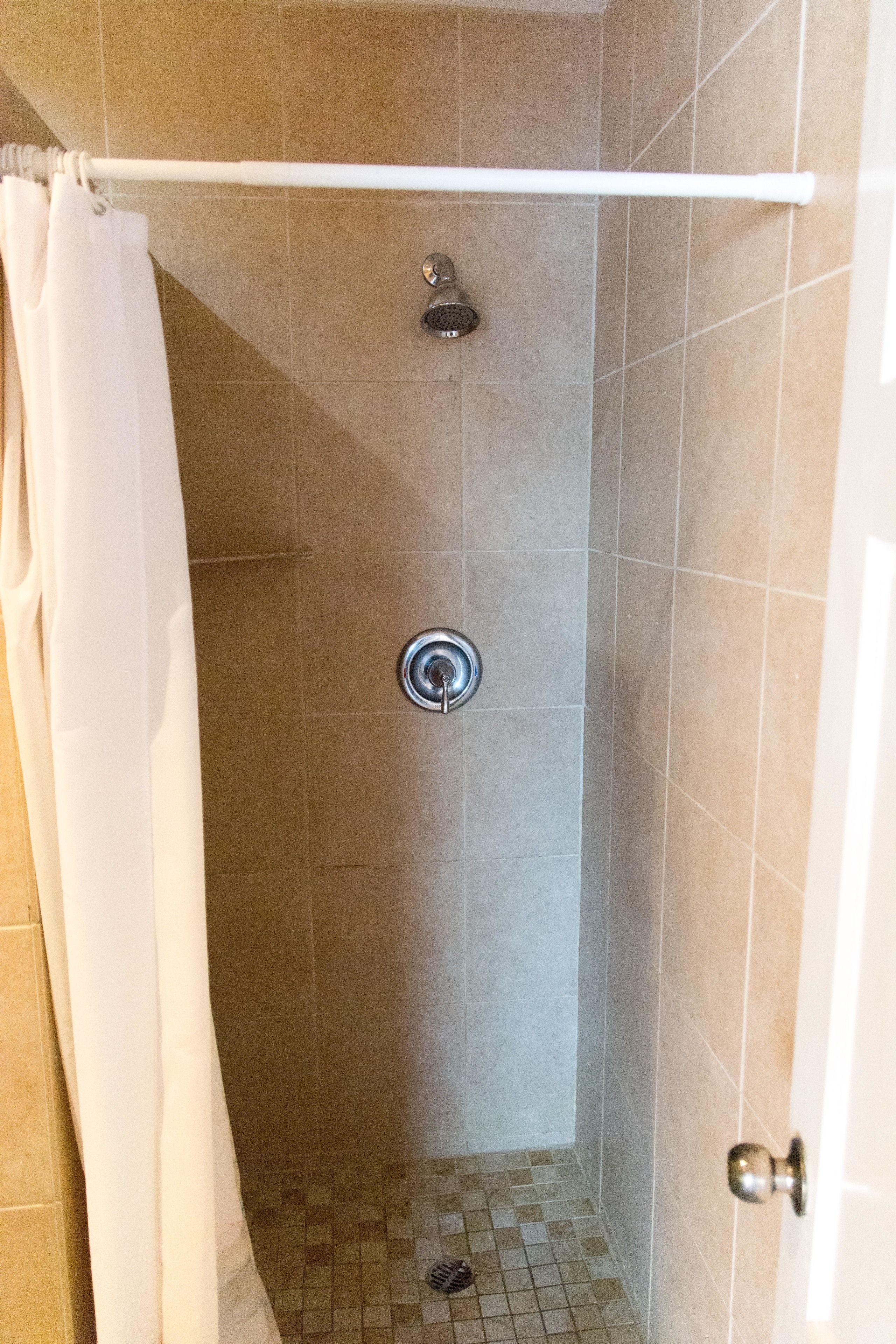 A shower with a white curtain, tiled walls, and a visible drain.