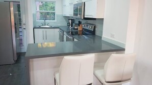 A modern kitchen with white cabinets, a stainless steel island, and a built-in oven. - HBK Villa Rentals at Jolly Harbour (Jolly Harbour)