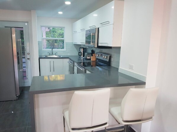A modern kitchen with white cabinets, a stainless steel island, and a built-in oven. - HBK Villa Rentals at Jolly Harbour (Jolly Harbour)