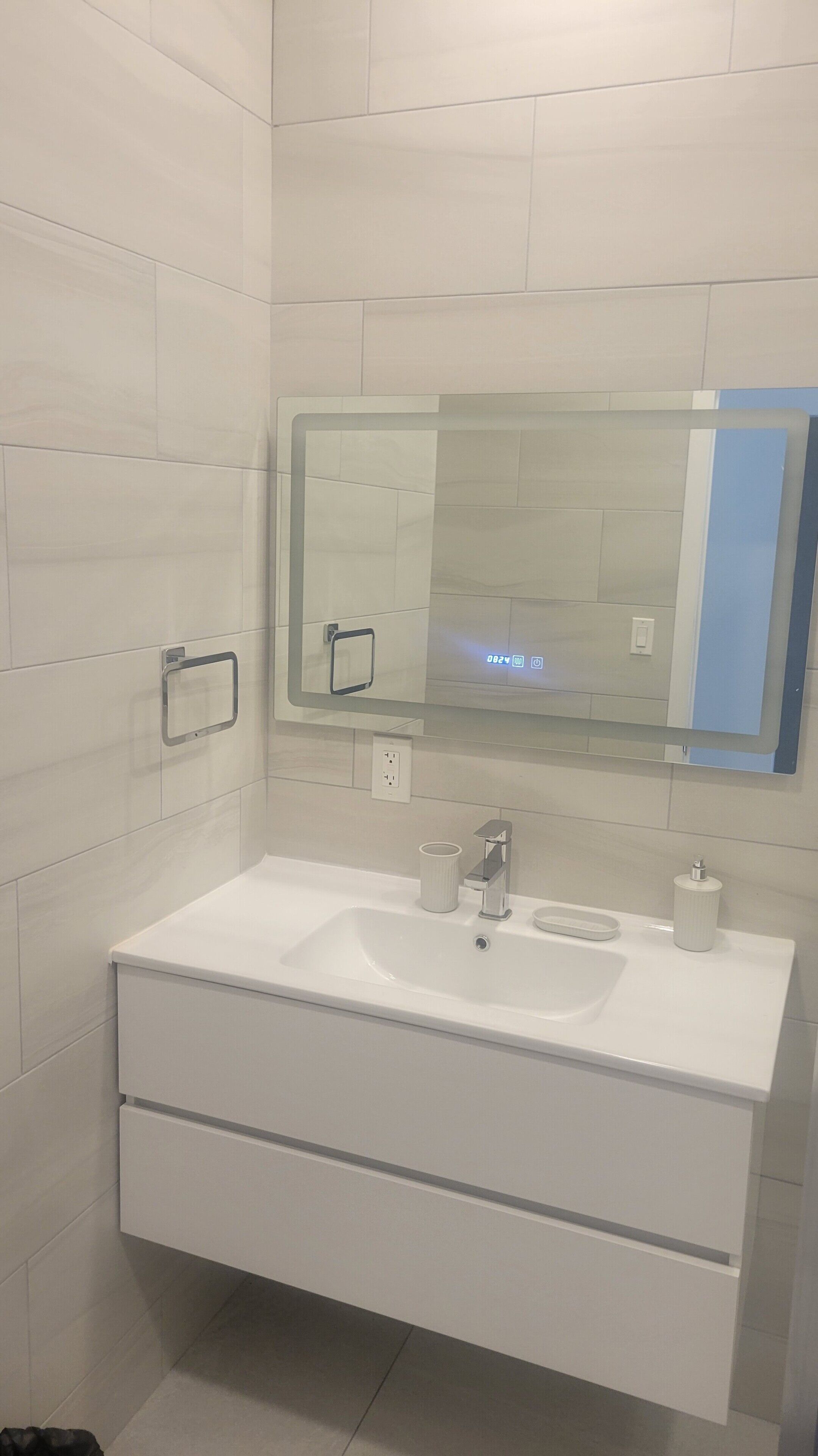 Un baño moderno con lavamanos, espejo y toallero blancos.