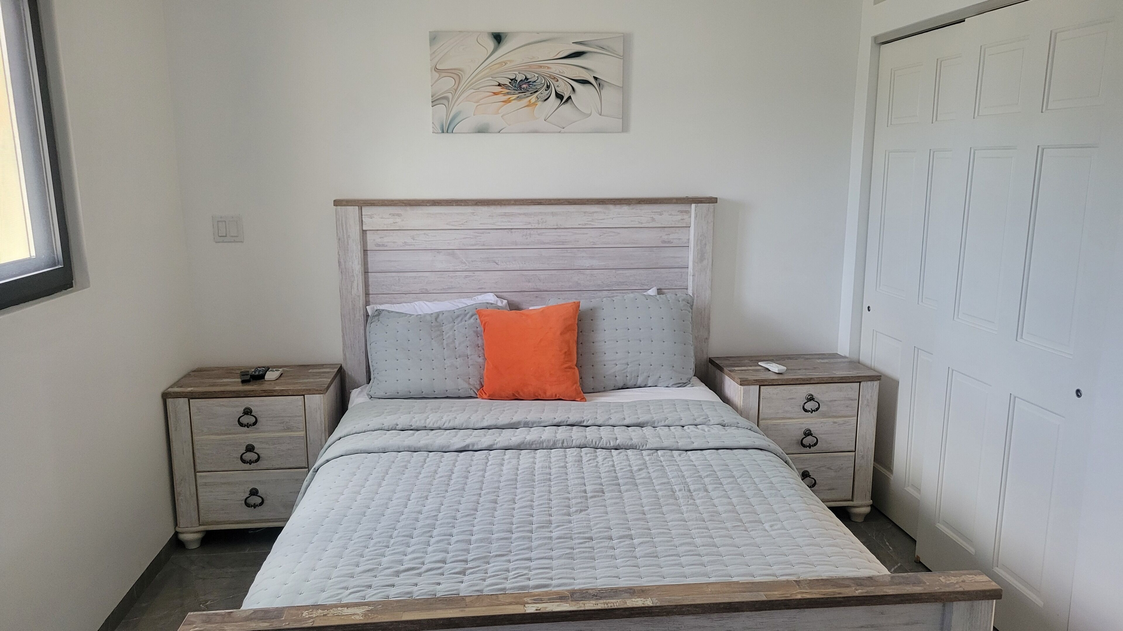 Une chambre à coucher avec un lit, deux tables de chevet, une tête de lit en bois, une œuvre d’art murale et une porte blanche.