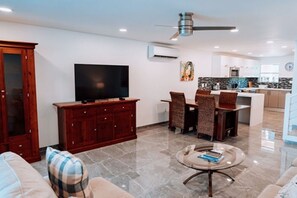 A modern living room with a flat-screen TV, a dining area, and a kitchen. - HBK Villa Rentals at Jolly Harbour (Jolly Harbour)