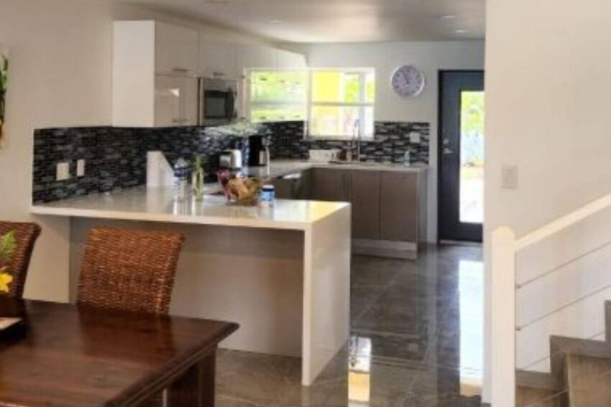 A modern kitchen with a central island, a dining area with a wooden table, and a staircase leading to another level.