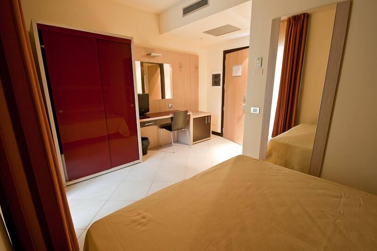 Una habitación de hotel con una cama, un escritorio, una silla, un armario y un espejo.