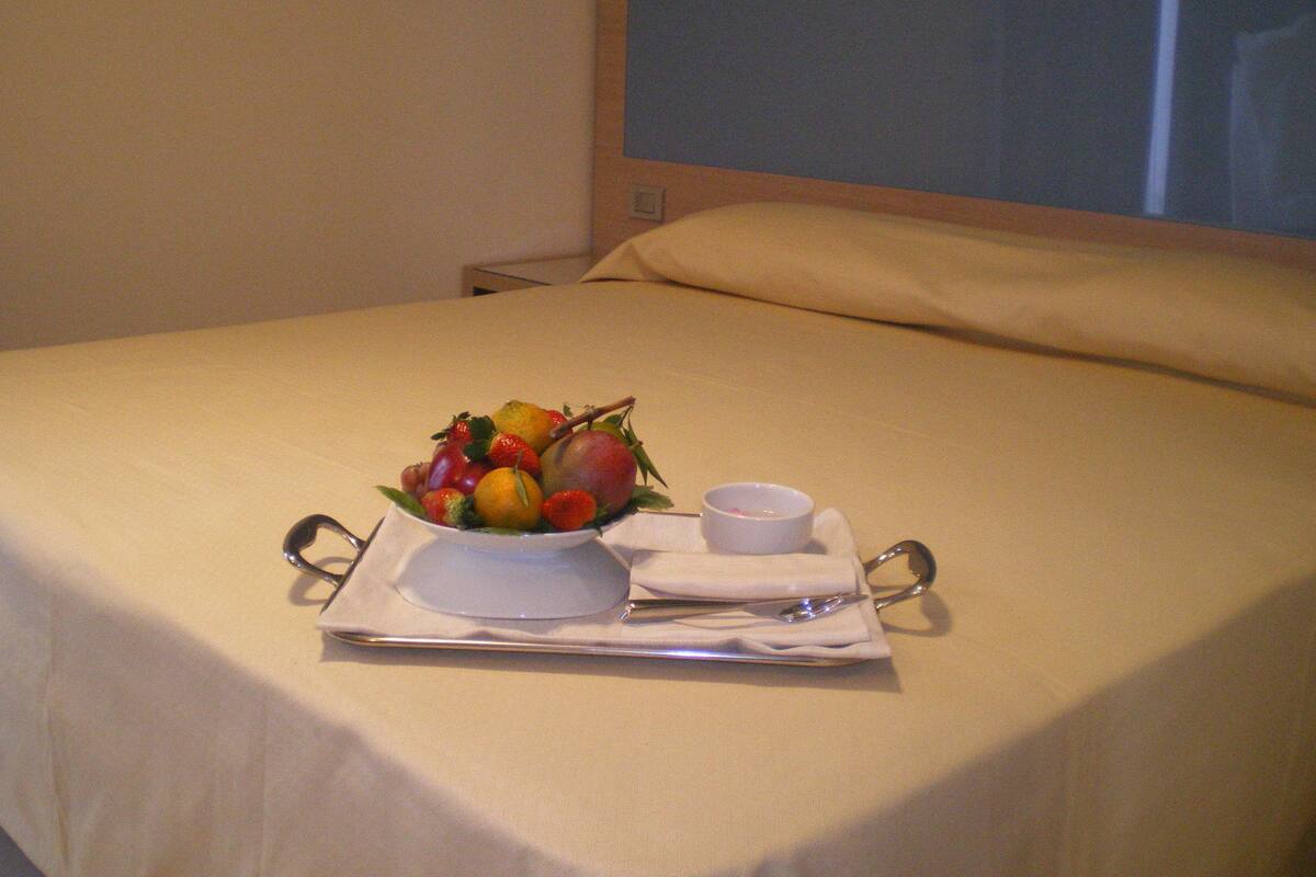 Una cama bien tendida con una bandeja de fruta y una taza de café sobre ella.