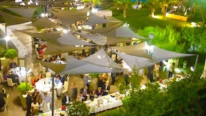 Un événement en plein air comprenant plusieurs espaces de restauration abrités par de grands parasols, le tout entouré de verdure et d’une piscine.