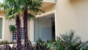 Un immeuble à plusieurs étages doté de balcons, d’un palmier et d’une entrée avec une porte en verre.