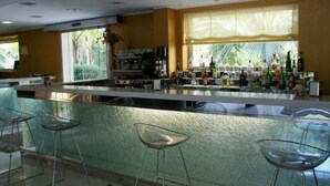 Un espace bar moderne doté d’un comptoir en verre, de tabourets de bar et d’une grande fenêtre offrant une vue sur la verdure.