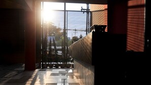 A corridor with a checkered floor pattern and a view of the outside through a window with blinds. - Serene at Chiang Rai (Chiang Saen)