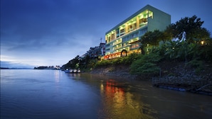 A modern hotel with multiple floors, a waterfront view, and a reflection of lights on the water. - Serene at Chiang Rai (Chiang Saen)
