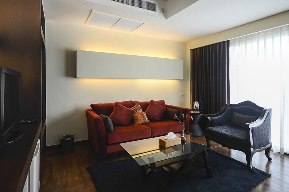 A modern living room with a red sofa, a black armchair, a glass coffee table, and a mounted TV.