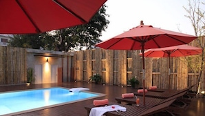 A wooden deck with a pool, red umbrellas, and lounge chairs. - Serene at Chiang Rai (Chiang Saen)