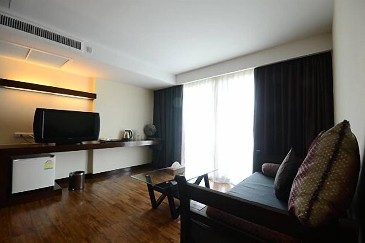 A modern hotel room with a flat-screen TV, a coffee maker, a sofa, and a large window with curtains.