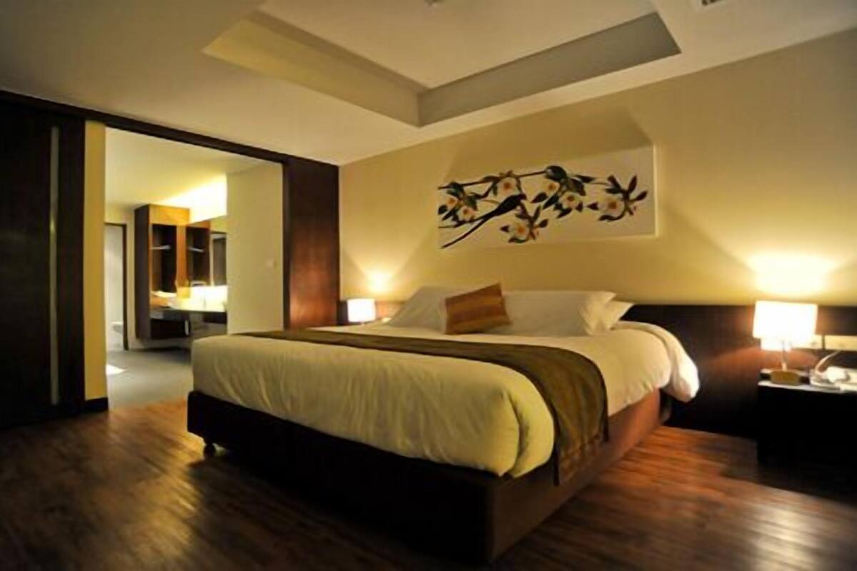 A modern hotel room with a large bed, a nightstand, a wall-mounted lamp, and a painting.