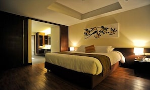 A modern hotel room with a large bed, a nightstand, a wall-mounted lamp, and a painting.