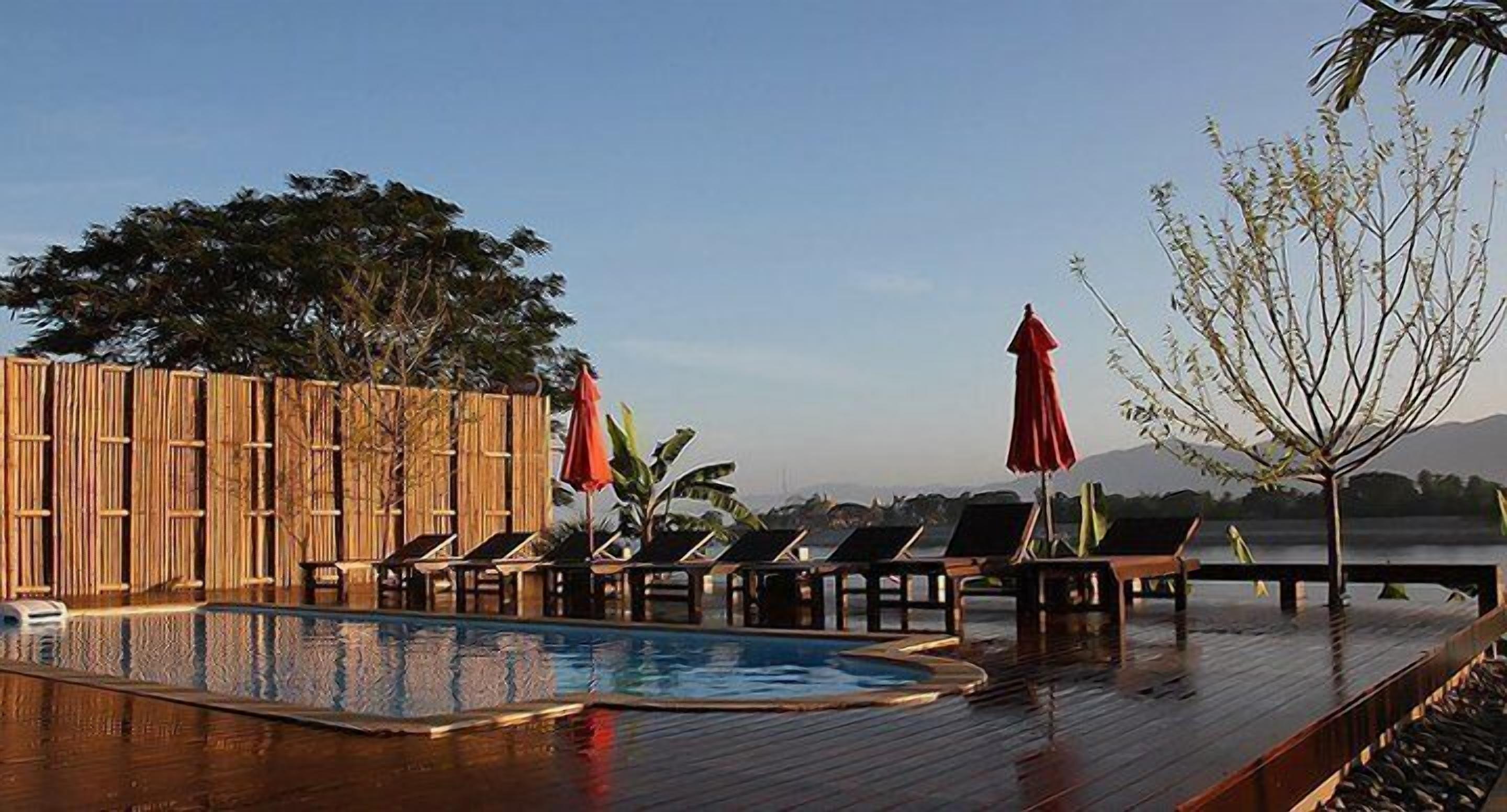 A wooden deck with a pool, lounge chairs, and umbrellas.