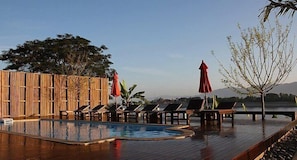 A wooden deck with a pool, lounge chairs, and umbrellas.