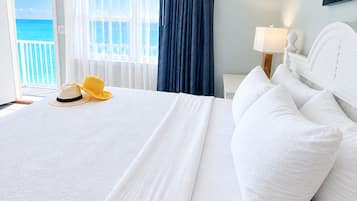 A hotel room with a bed, a nightstand, a lamp, a painting, and a view of the ocean.