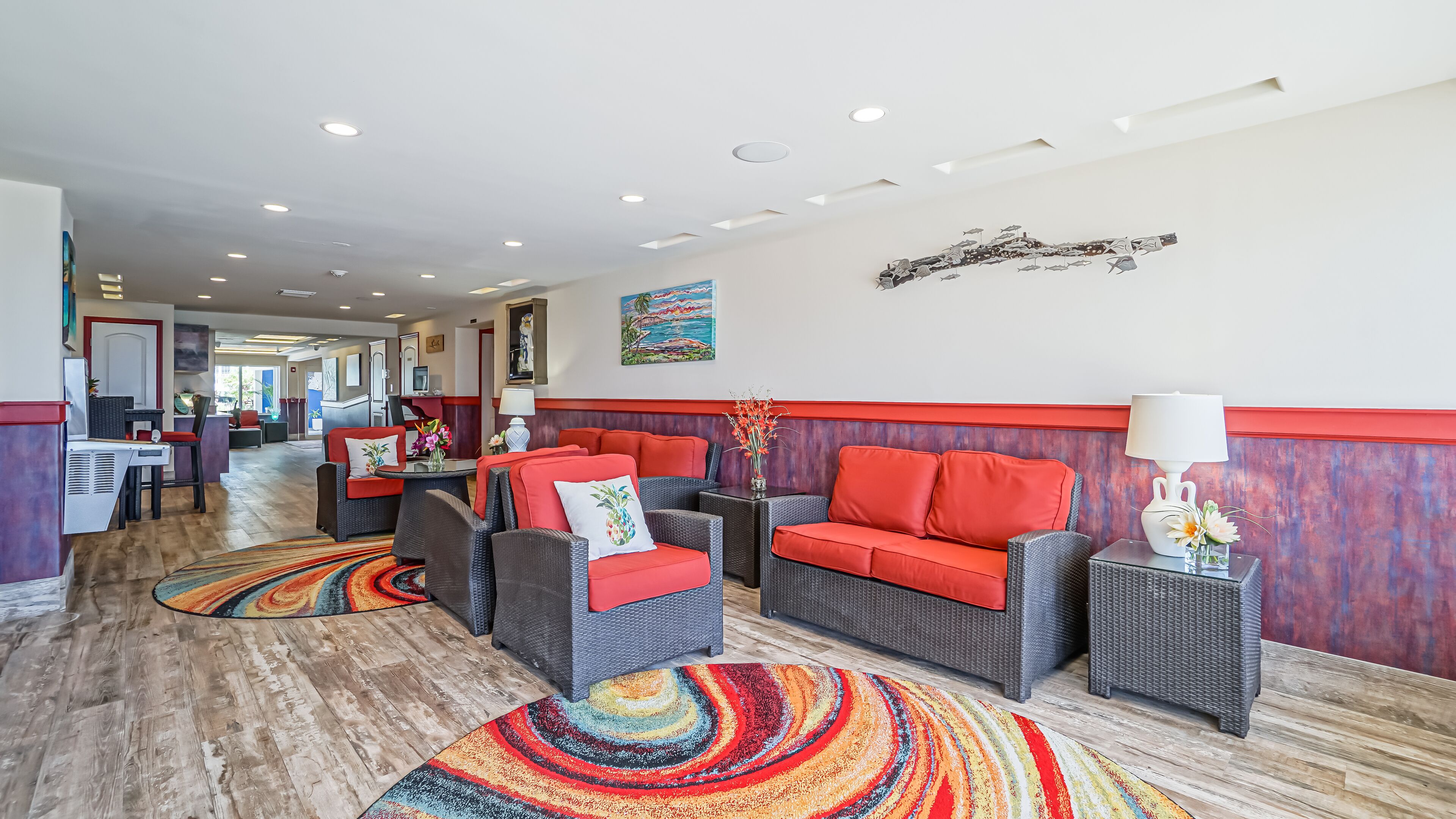 A hotel lobby with wicker furniture, a colorful carpet, and a painting on the wall.