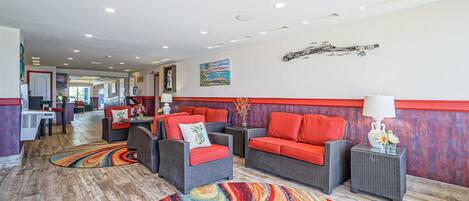 A hotel lobby with wicker furniture, a colorful carpet, and a painting on the wall.