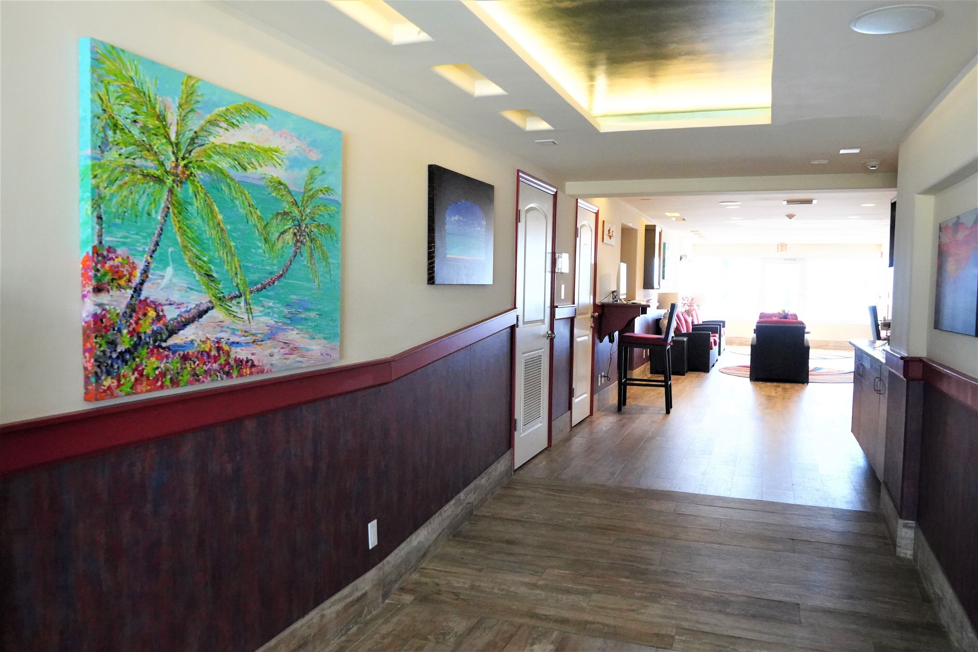 A hotel hallway with a wooden floor, a large tropical mural, and a reception area in the distance.