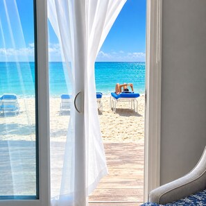 A beach view through a window with white curtains, a wooden deck, and beach chairs. - Glunz Ocean Beach Hotel & Resort (Key Colony Beach)