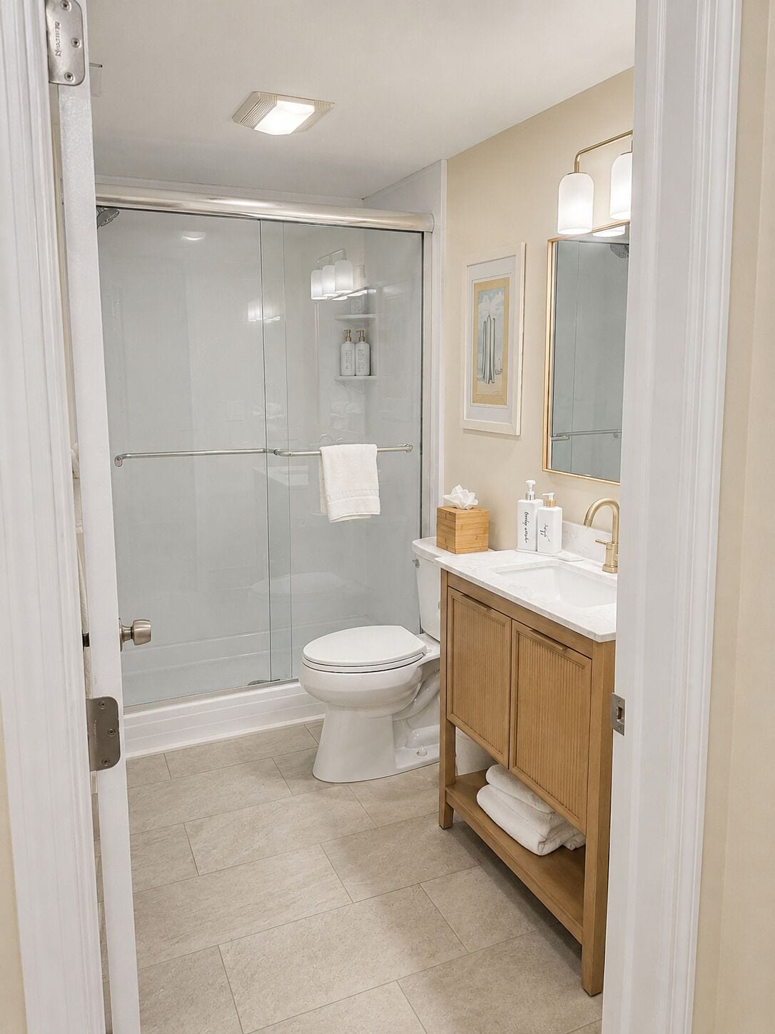 A bathroom with a glass-enclosed shower, a toilet, a vanity with a mirror, and a framed picture on the wall.