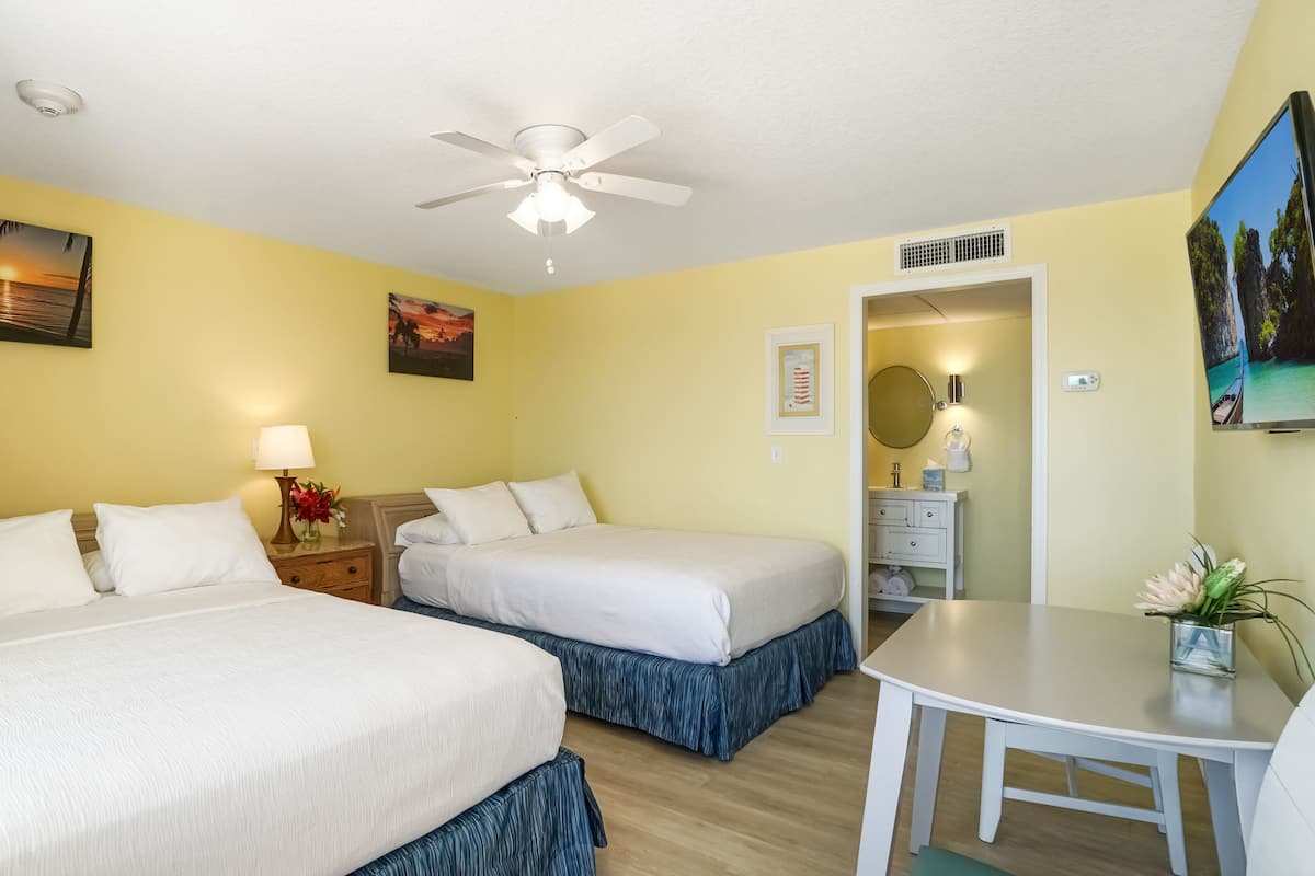 A hotel room with two beds, a ceiling fan, a desk, and a bathroom visible through an open door.
