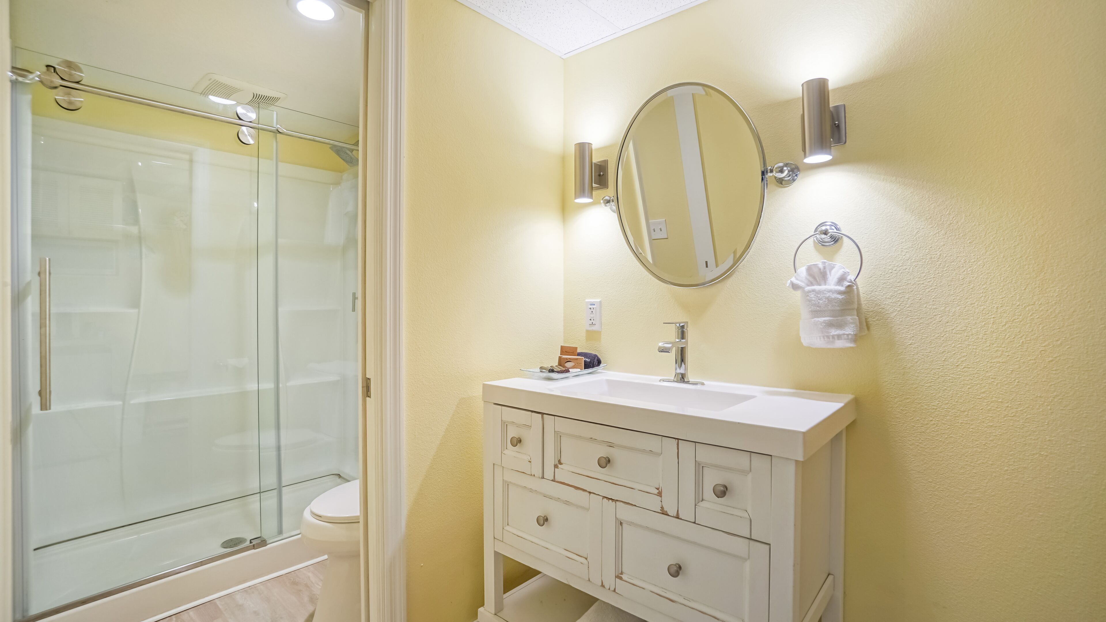 Un baño con cabina de ducha de vidrio, un lavabo blanco con espejo y un perchero para toallas.